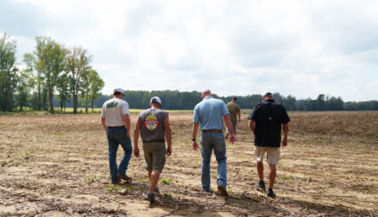 Five individuals walking in a farmer’s field looking down at the soil.